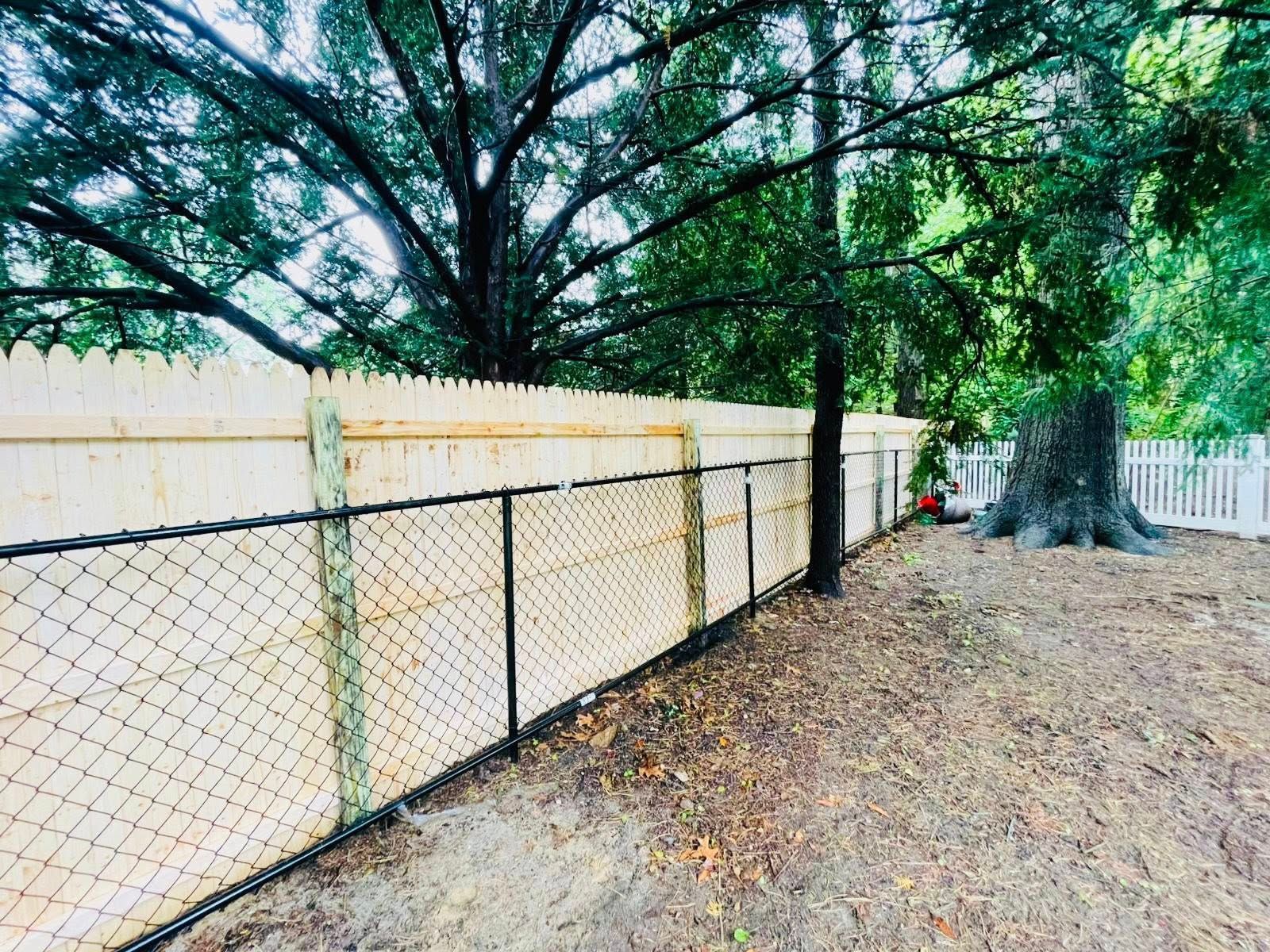 Chain link fence with a wooden fence on top, under trees.