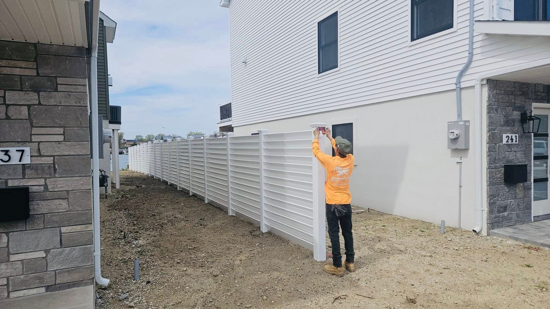 Man installing a white horizontal slat fence between two buildings. Construction site, outdoor setting.