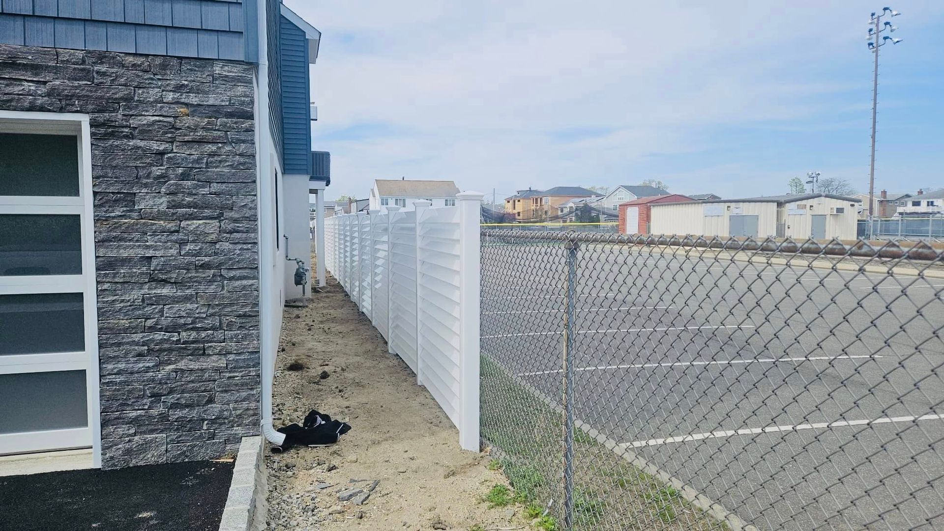 Exterior view of a building with stone siding next to a white fence, chain-link fence, and a road.