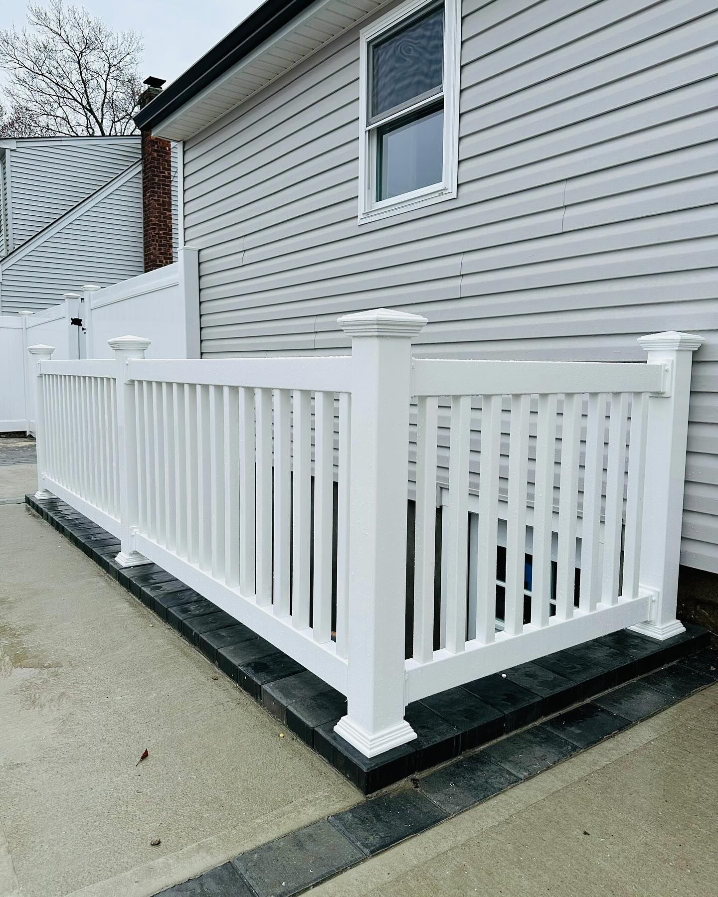 White picket fence surrounds a small, recessed area against a house with light gray siding.