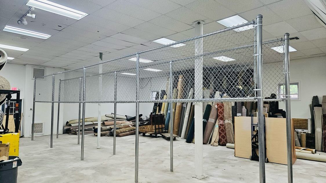 Chain-link fence structure inside a large, empty room with concrete flooring and exposed ceiling beams.