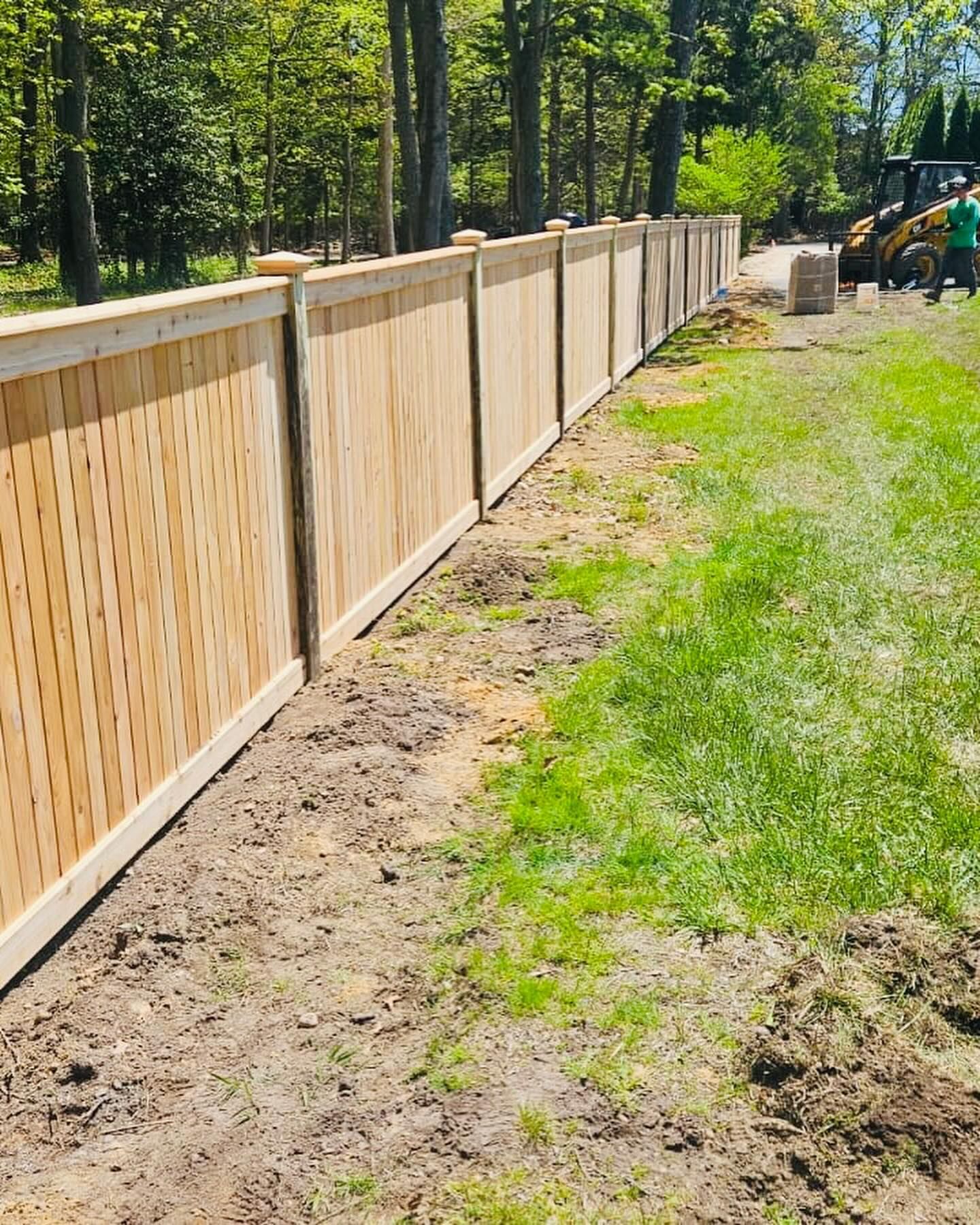 Wooden fence along a grassy area, trees in the background, a tractor in the distance.
