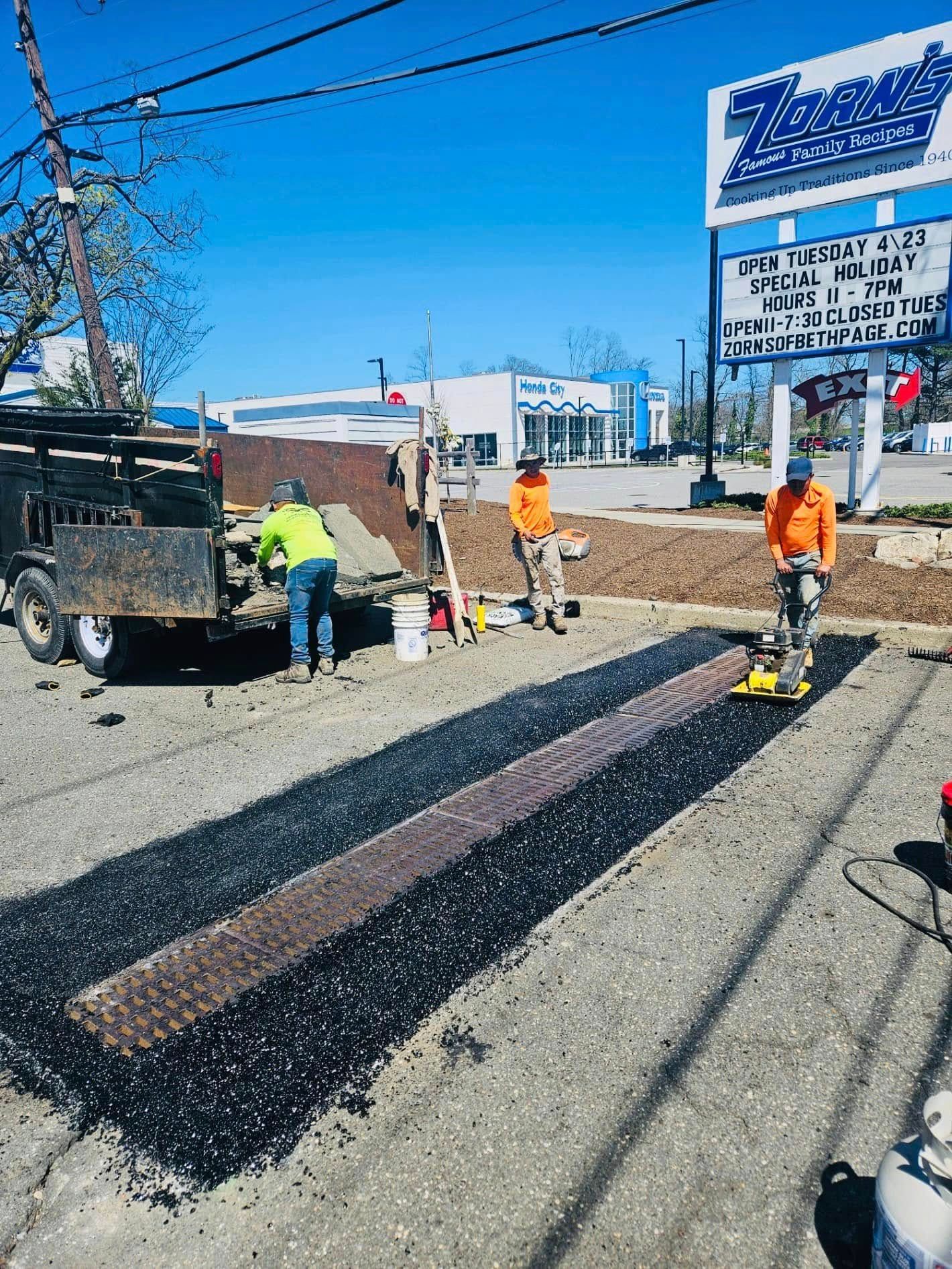 Road workers paving a street, with one compacting asphalt with a machine under a blue sky.