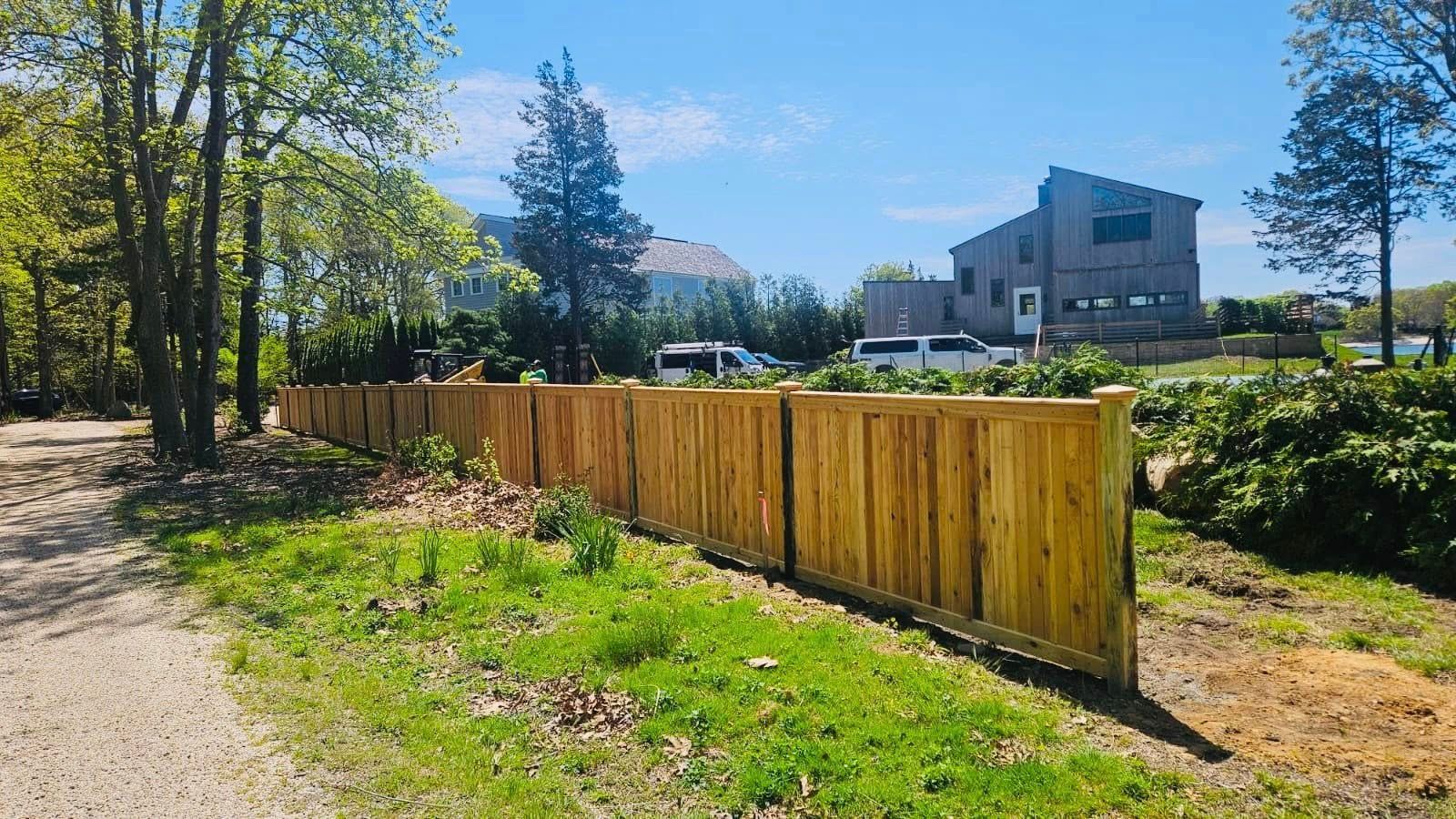 Wooden fence in a sunny outdoor setting with a gravel path, green grass, and trees.