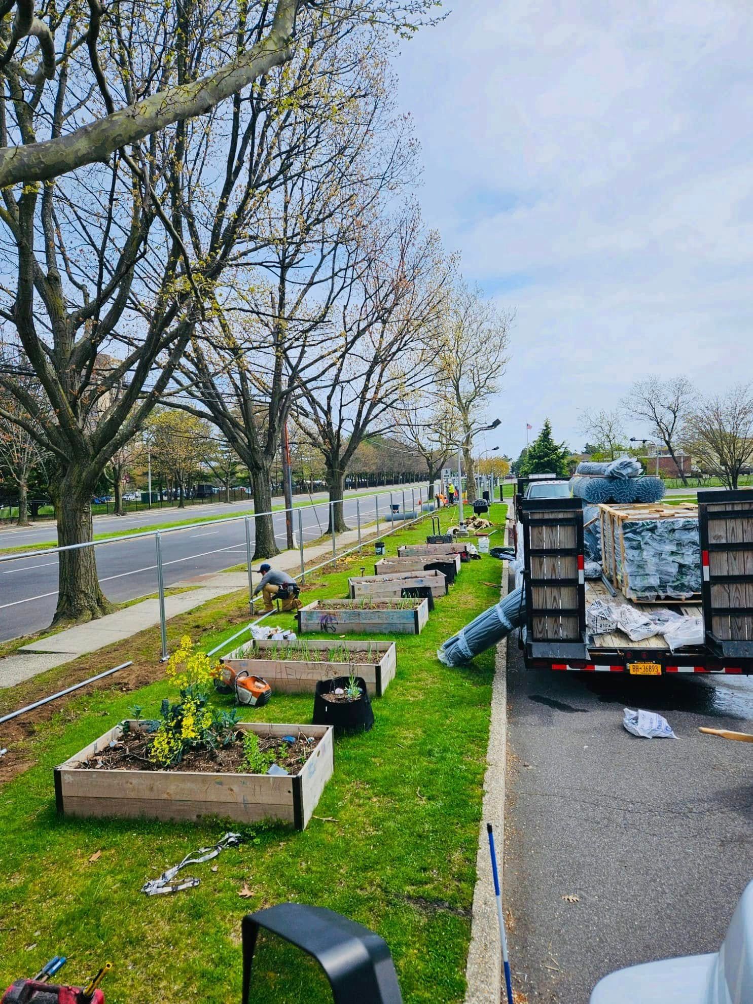 Raised garden beds along a road, being worked on. A truck with supplies is parked beside them.