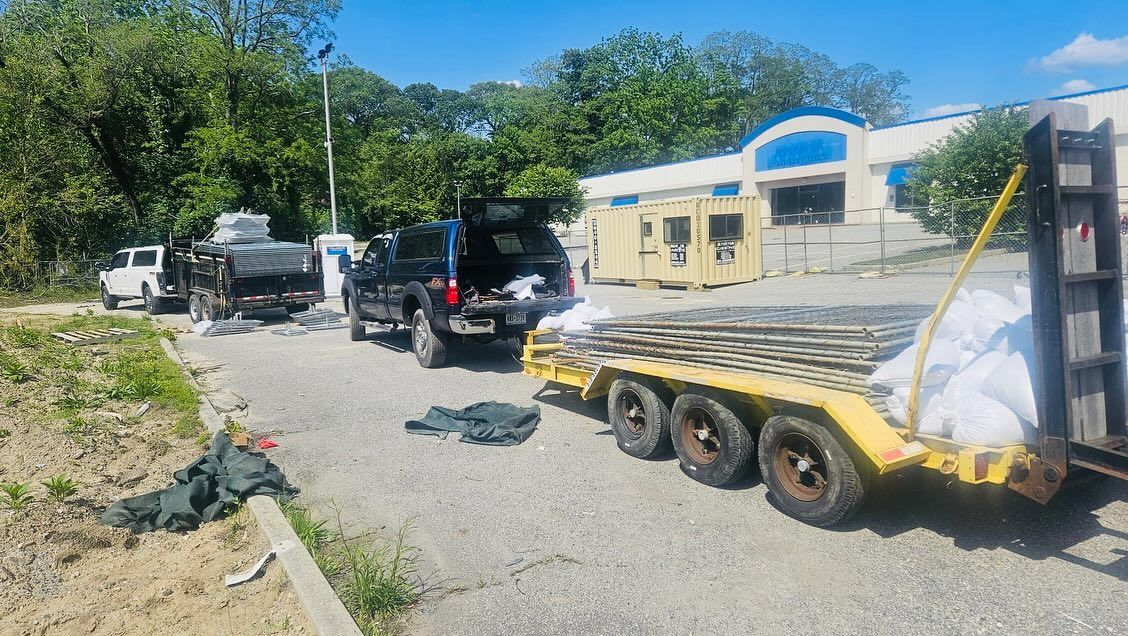 Cars and trailer parked on gravel near a building. Items are being unloaded, blue sky visible.