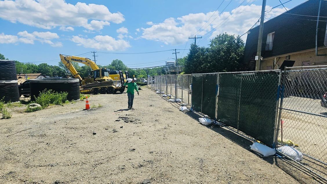 Construction site with a chain-link fence, a worker, and heavy machinery under a sunny sky.