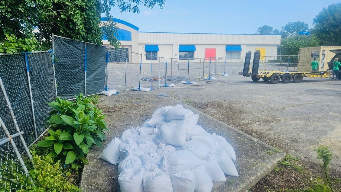 Bags of white material in front of a building with blue and yellow accents. Construction site with fencing.