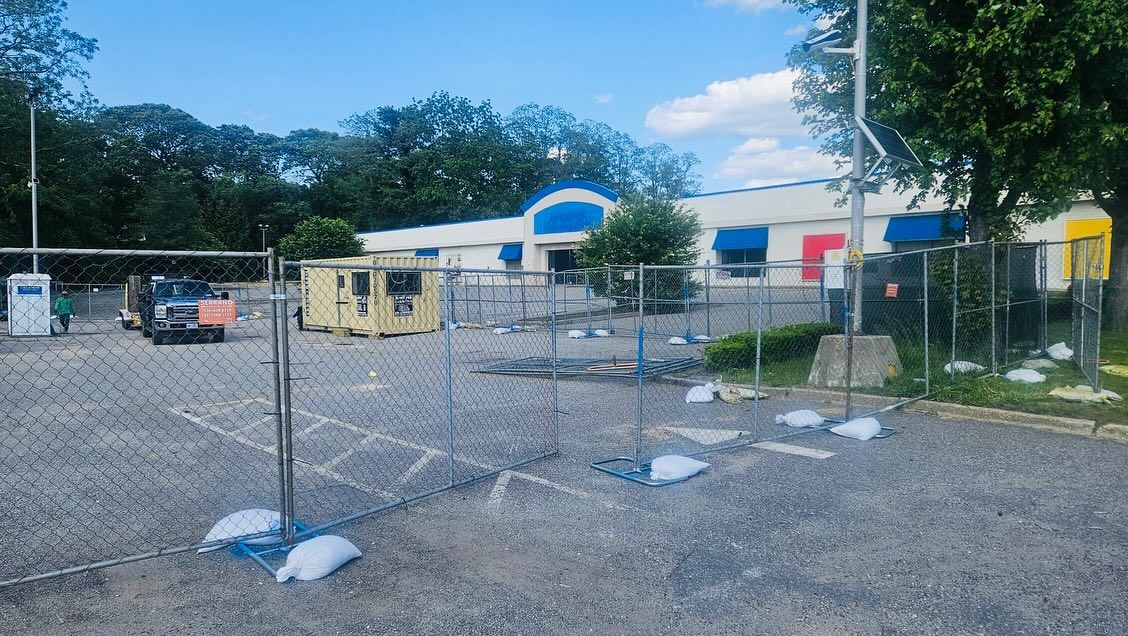 Exterior of building under construction with a chain-link fence, generator, and gravel.