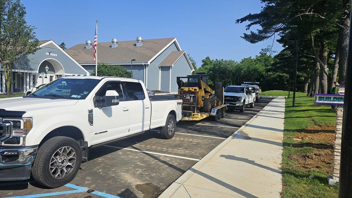 White pickup truck pulling equipment trailer parked near a building.