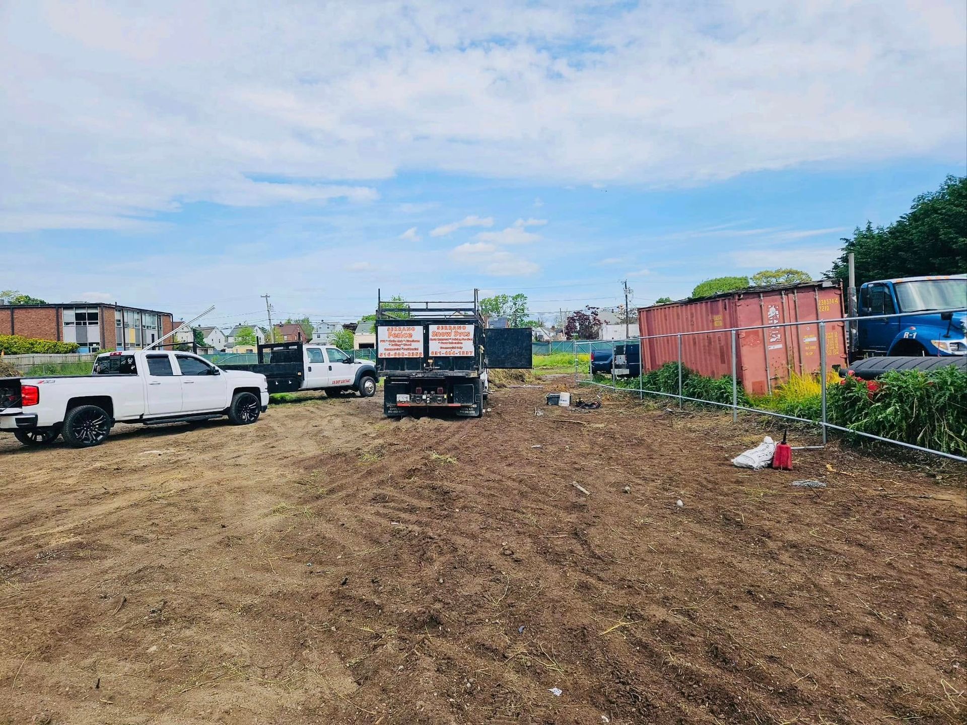 Dirt lot with several trucks and storage containers under a cloudy sky.