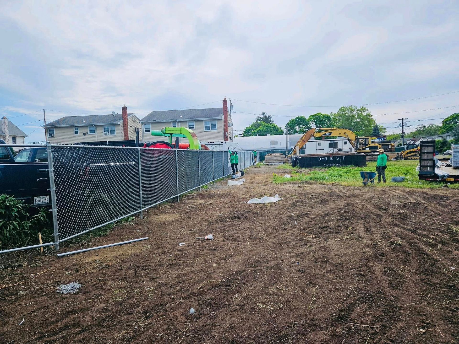 Construction site with chain link fence, two workers, and heavy machinery.