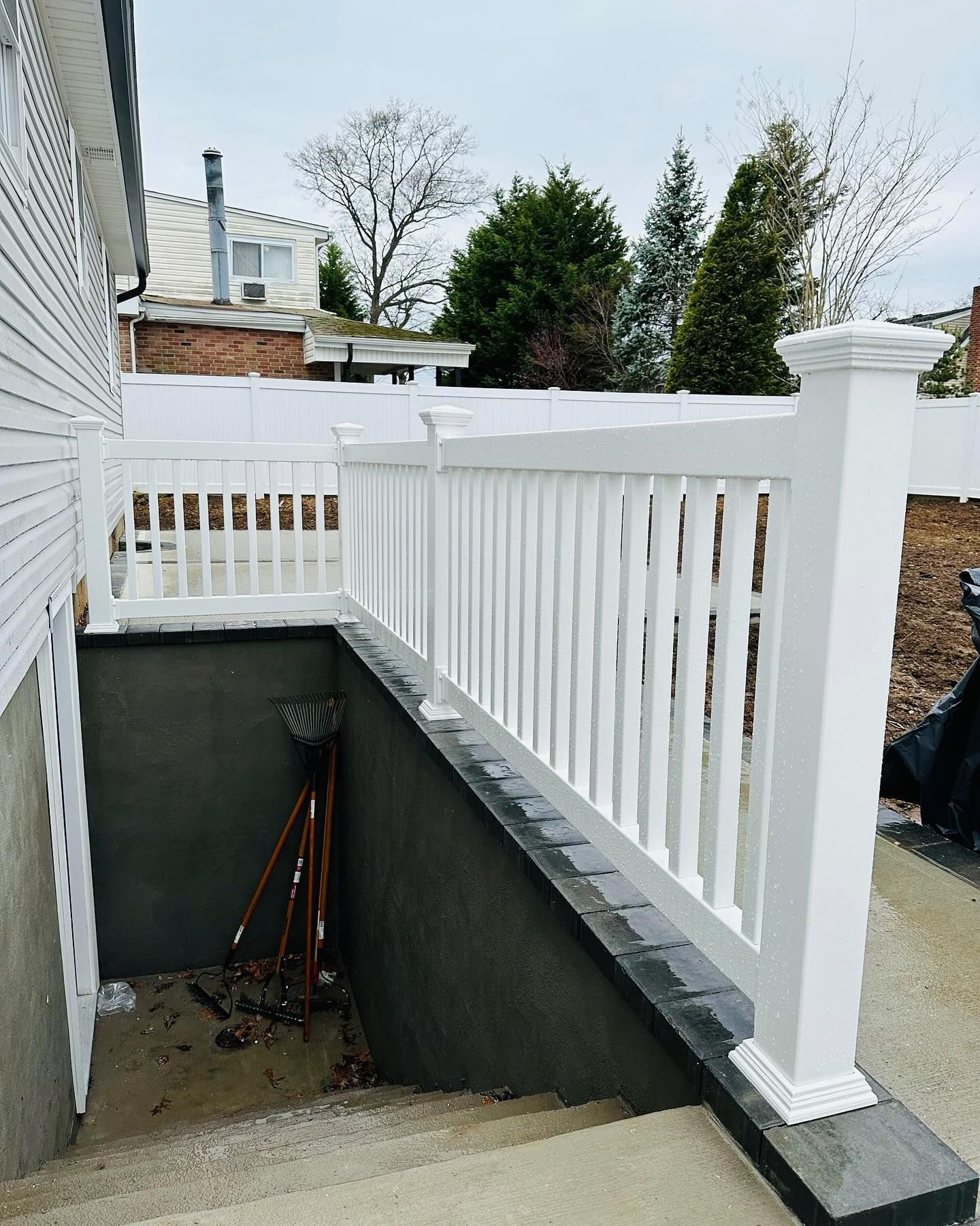 White railing on a dark gray concrete wall, leading to steps, next to a building.