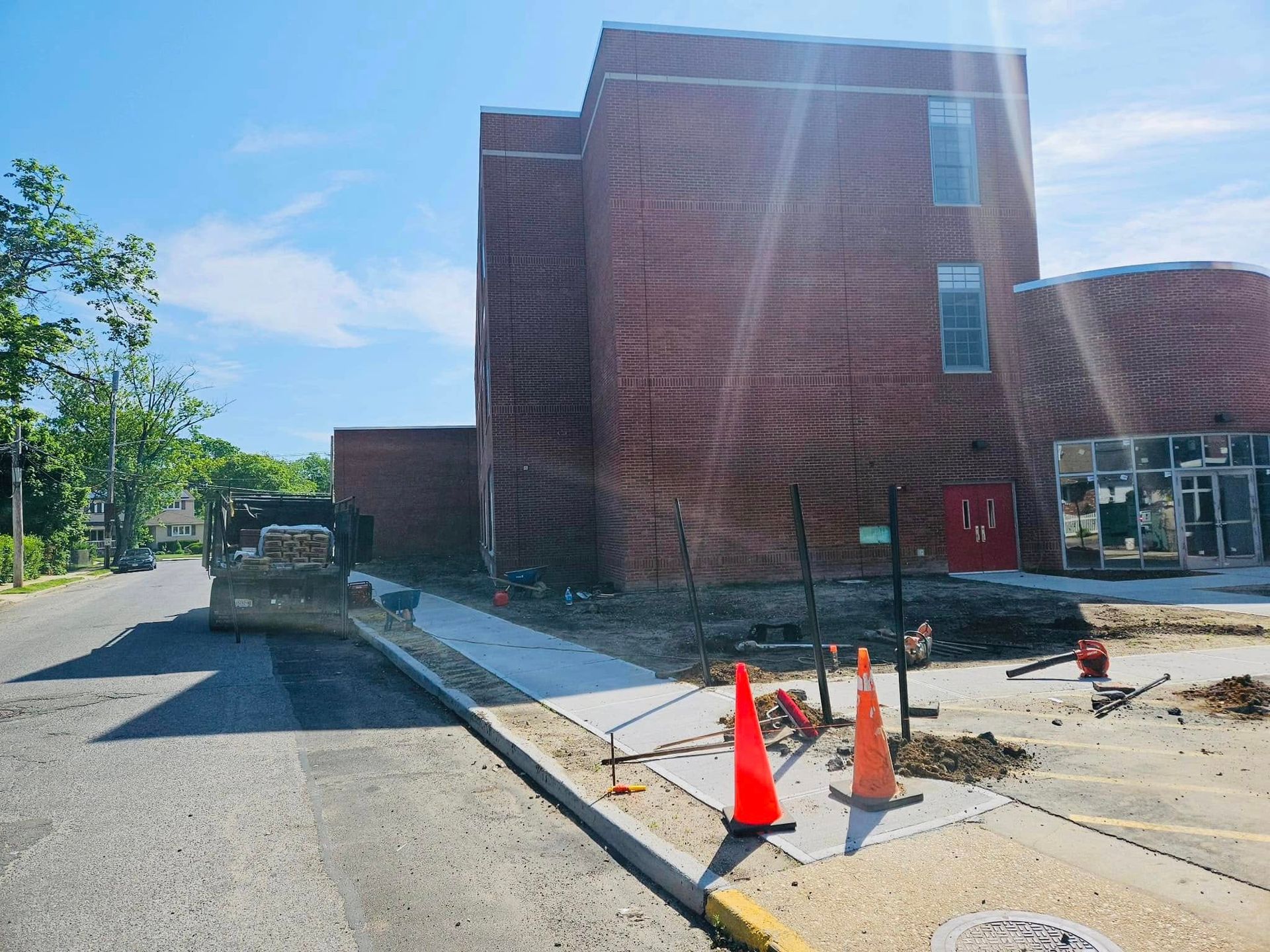 Brick building under construction, sidewalk with orange cones, sunny day.