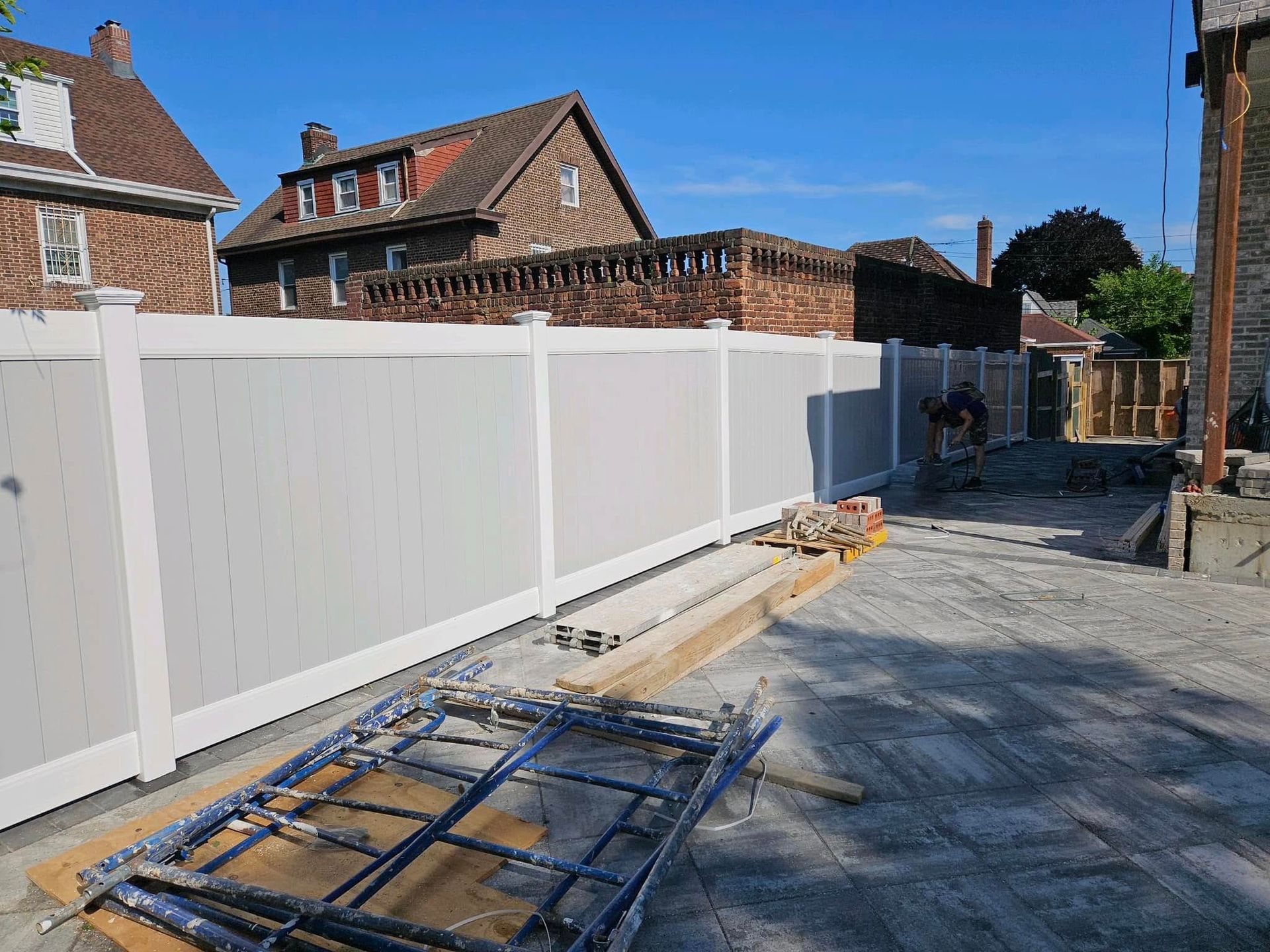 White and gray vinyl fence in front of brick buildings and a clear blue sky.