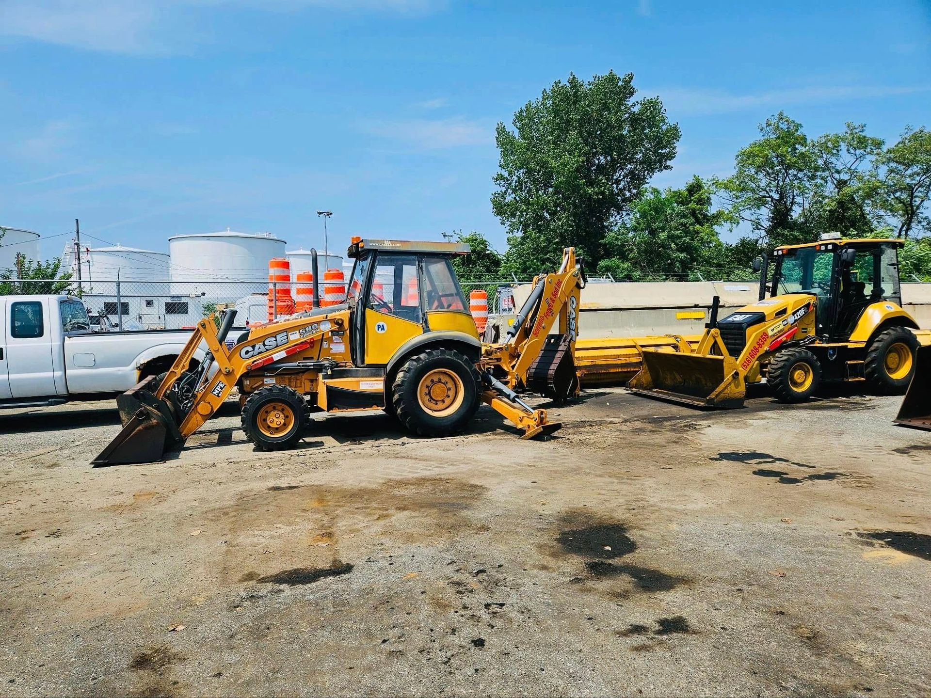 Two yellow Case backhoe loaders parked on gravel in a sunny outdoor setting.