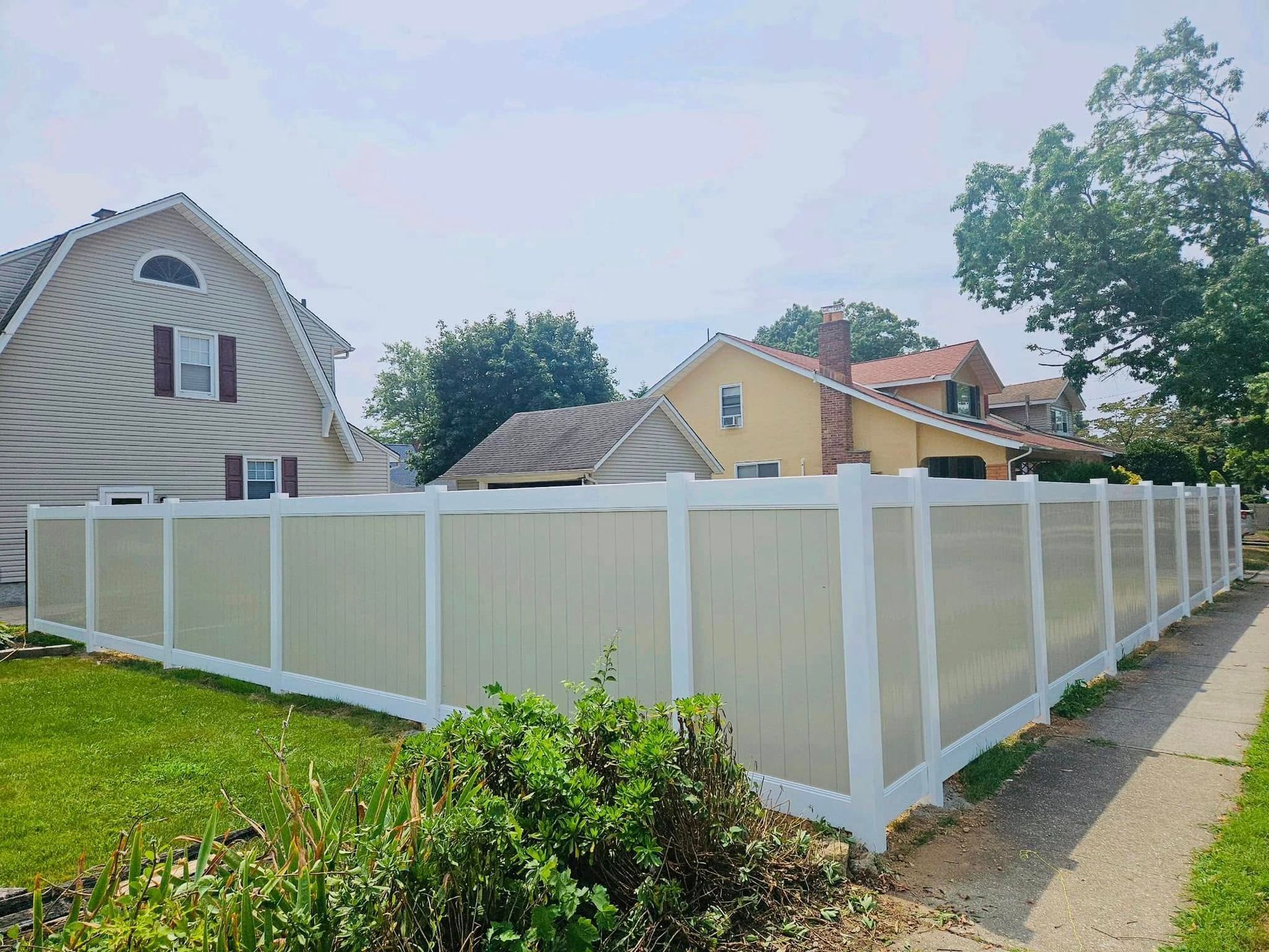 Tan and white vinyl fence around a yard with a grassy lawn, near houses and a sidewalk.