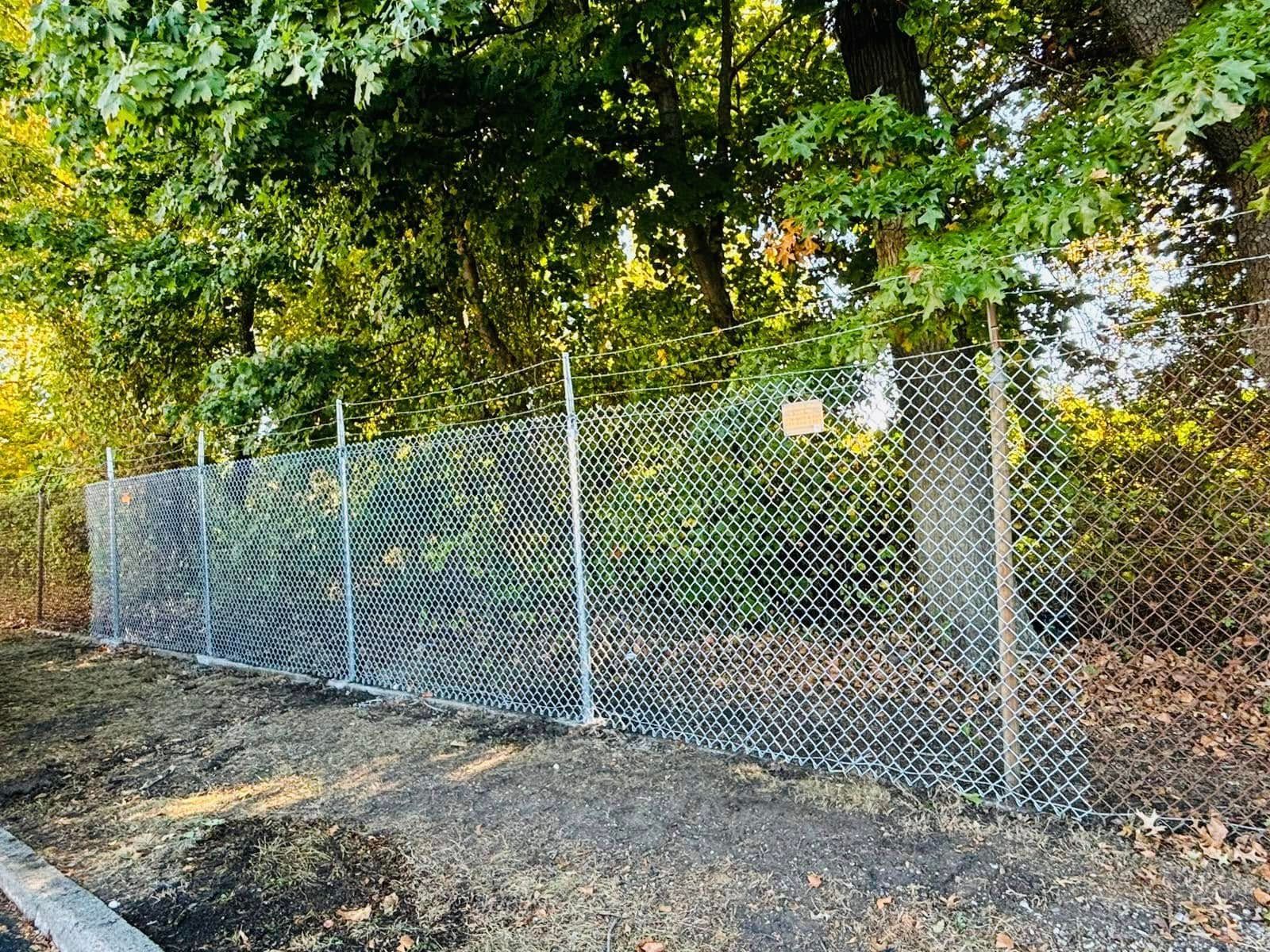 Chain-link fence in front of trees, set in a grassy area.