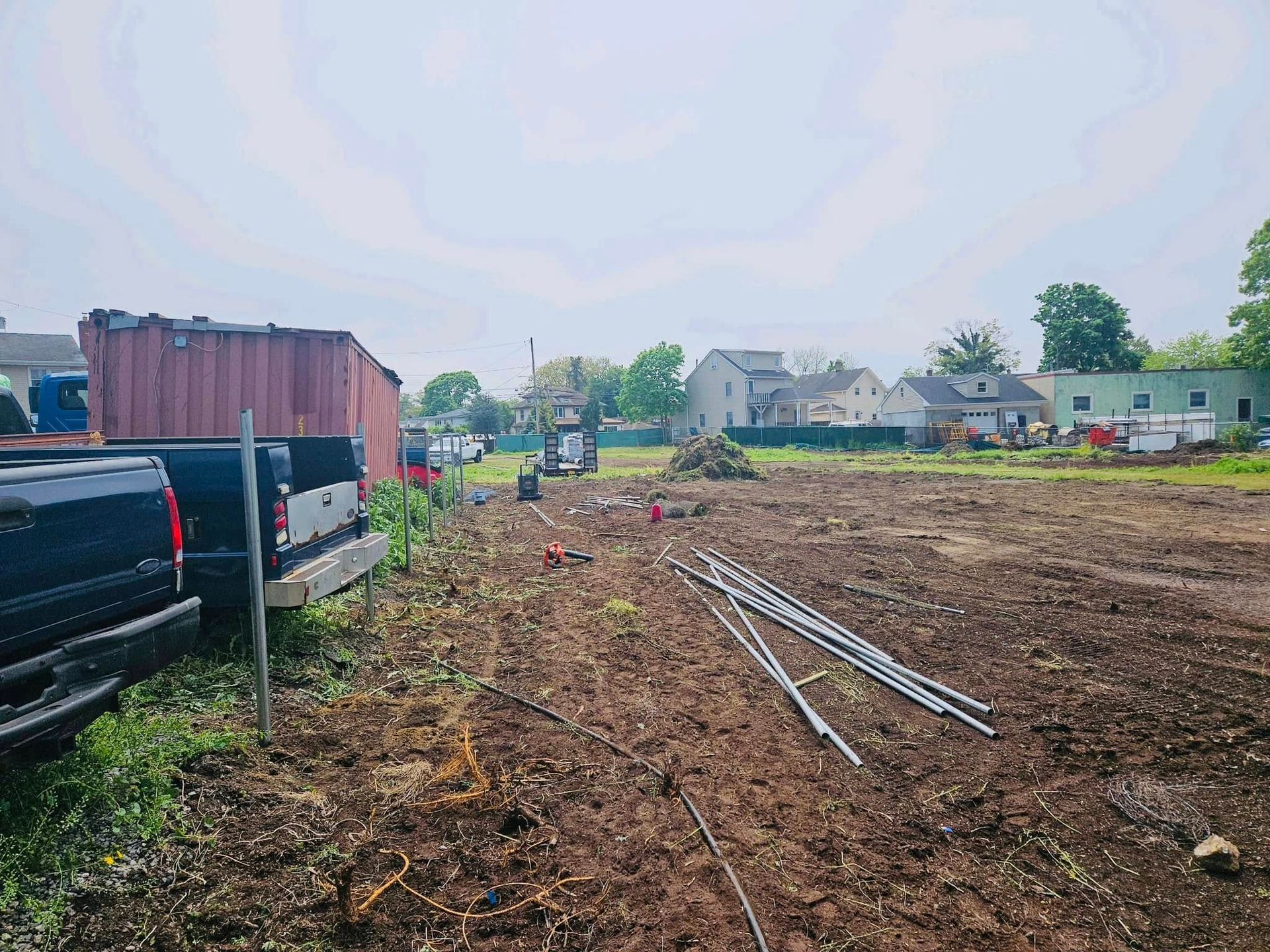 Construction site: dirt ground, equipment, metal poles, trucks, buildings in background.