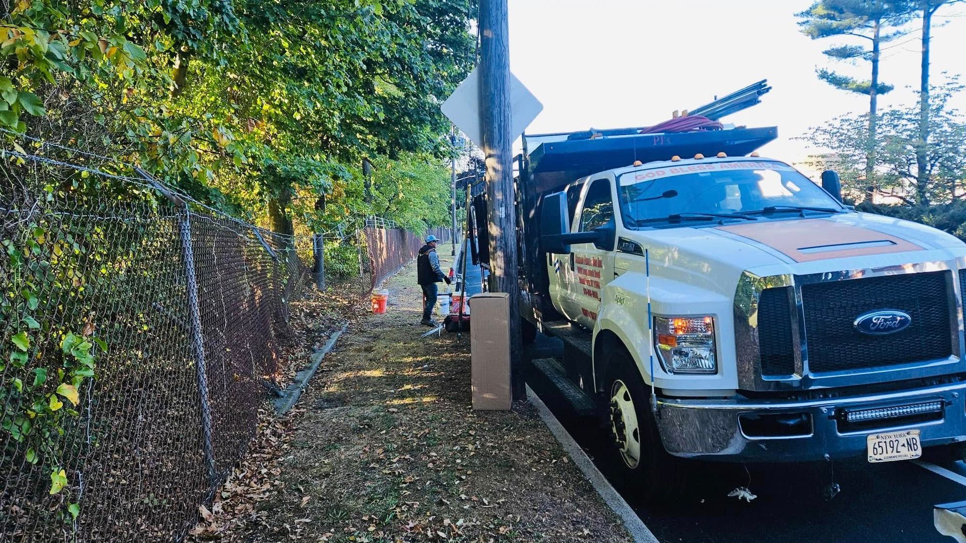White utility truck parked next to power pole, two workers on sidewalk.