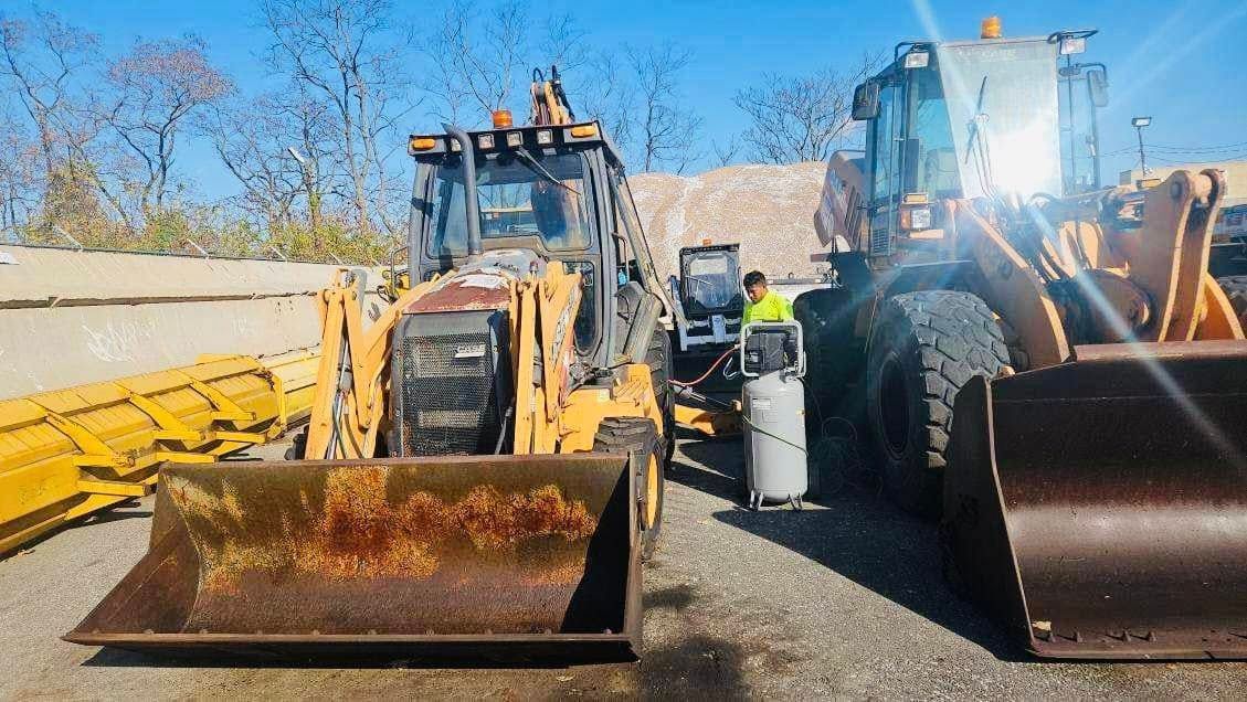 Two yellow construction vehicles, a backhoe and a loader, parked outside. A person is working between them.