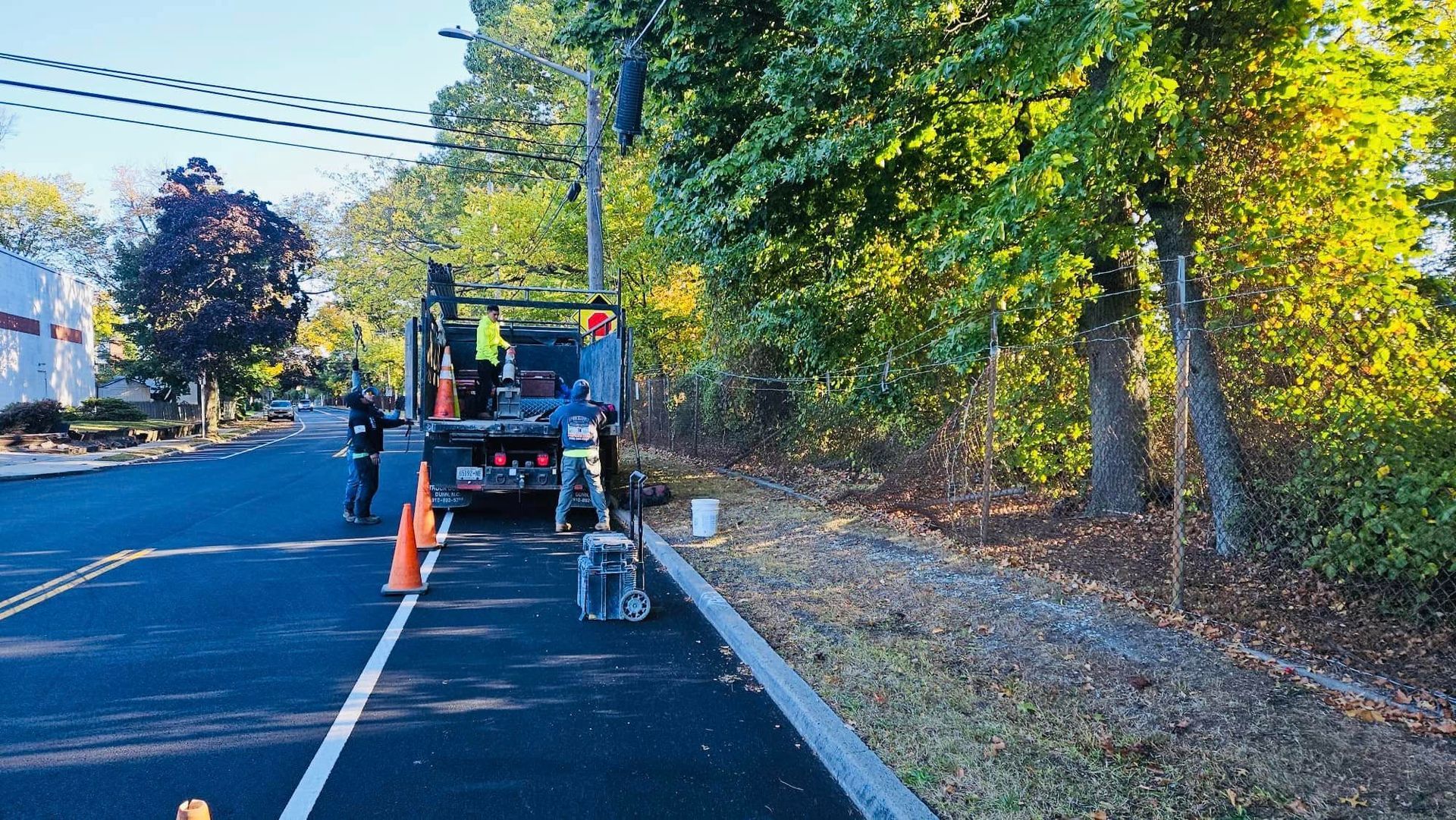 Utility truck parked on road near trees, workers present; road work in progress.