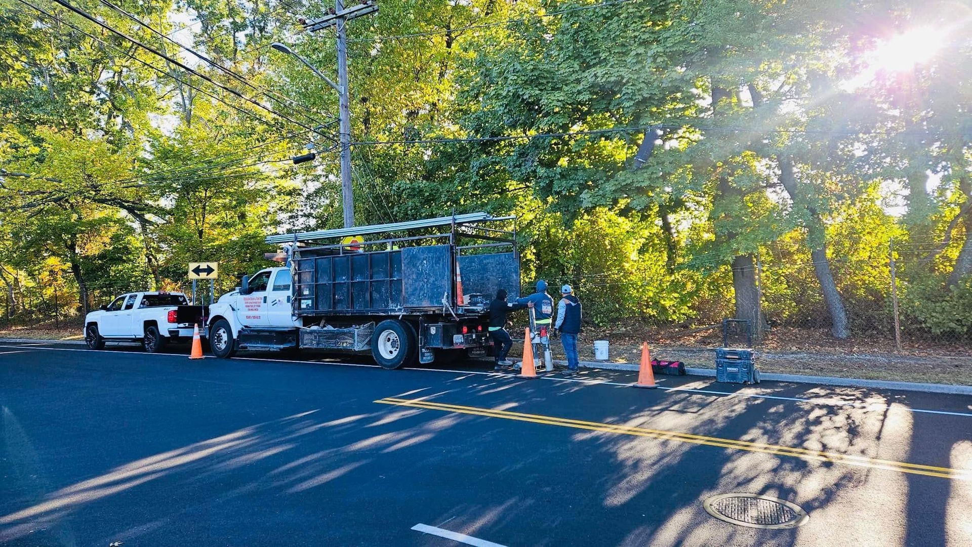 Utility workers and trucks on a road next to power lines, repairing infrastructure. Sunny day.