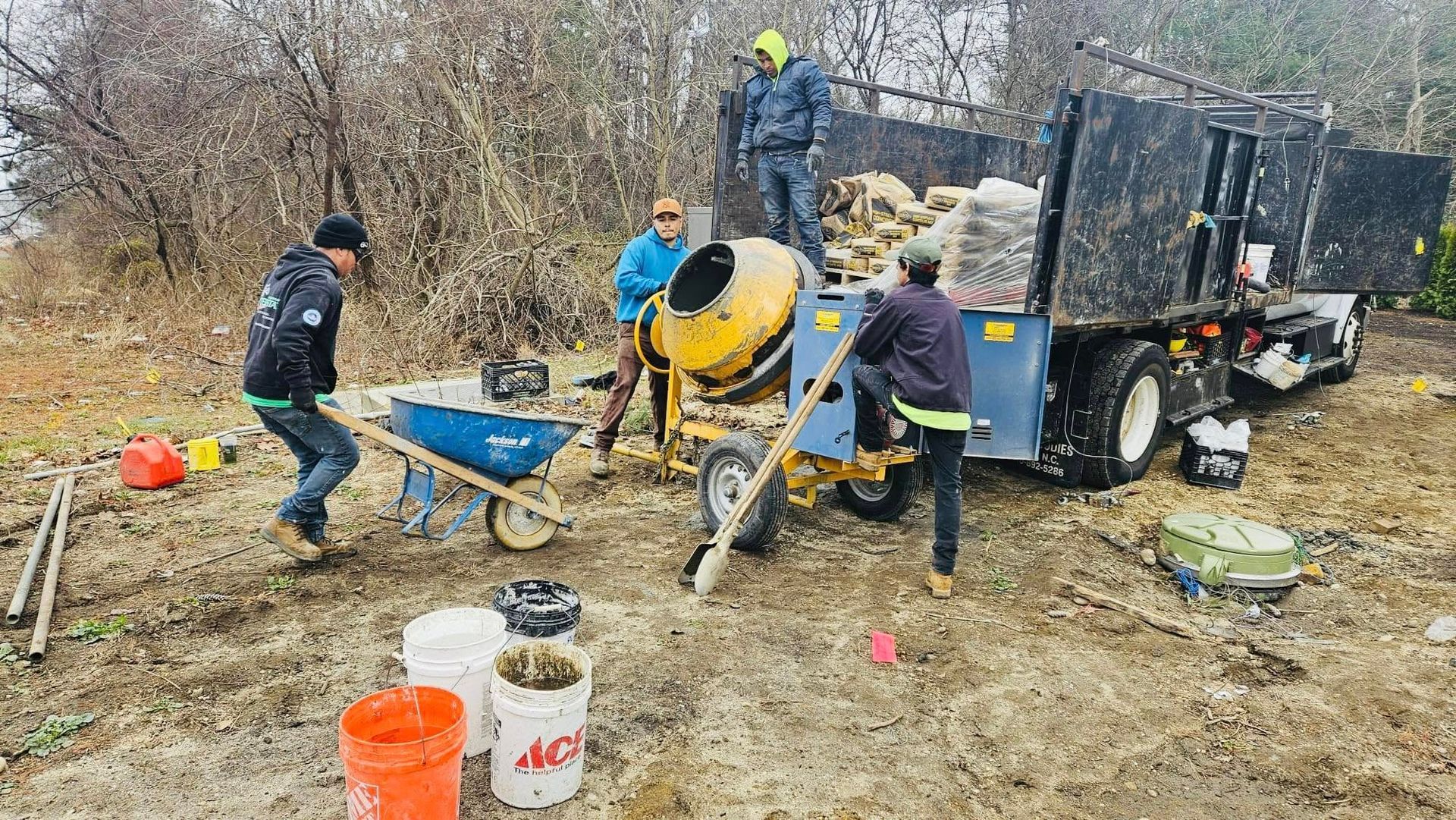 Construction workers mixing cement near a truck, in a muddy outdoor setting.
