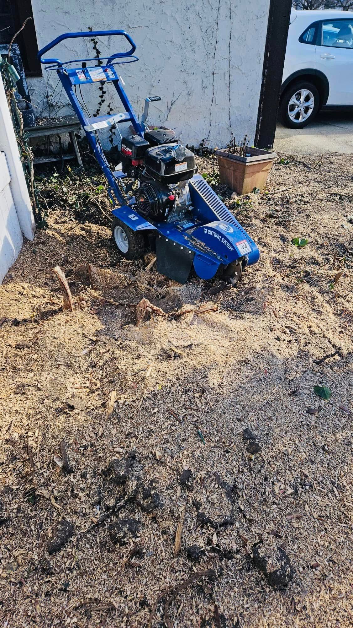 Blue rototiller tilling a patch of soil in front of a building.