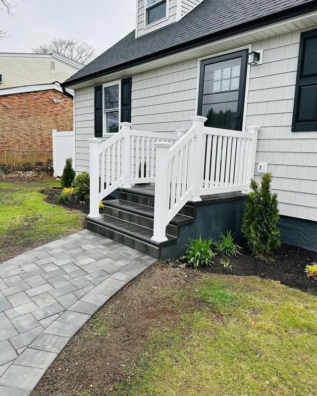 Front porch with white railings, black steps, and a gray stone walkway beside a light gray house.