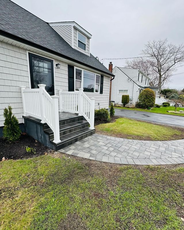 Small gray house with white porch steps, dark shutters, and a curved stone walkway on a cloudy day