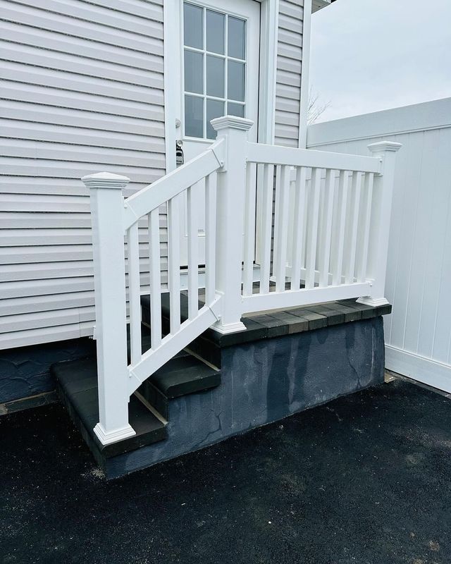 White porch stairs and railing beside a house entrance with black foundation trim