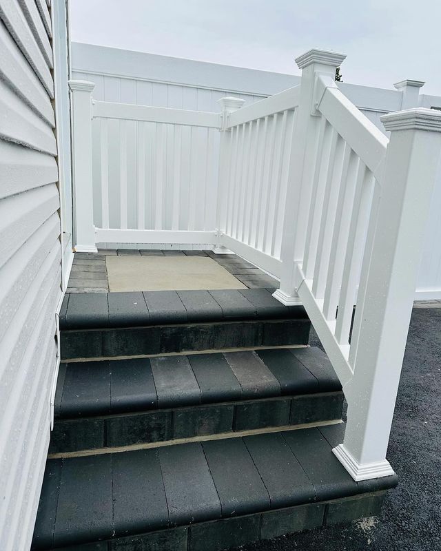 White stair railing with black steps leading to a fenced outdoor landing.