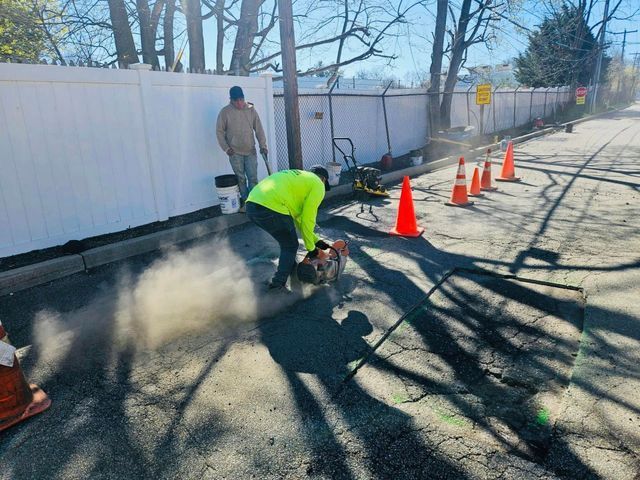 Road worker cutting pavement with a saw near orange cones and dust on a sunlit street