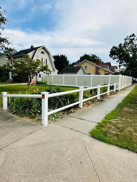 White fence along a sidewalk beside suburban houses and green yards under a partly cloudy sky