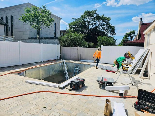 Workers installing a backyard in-ground pool beside a white fence and paving stones
