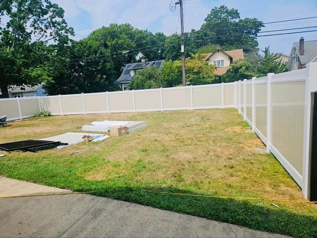 Backyard with white vinyl fence, patchy grass, concrete patio, and a small paved area near a utility pole