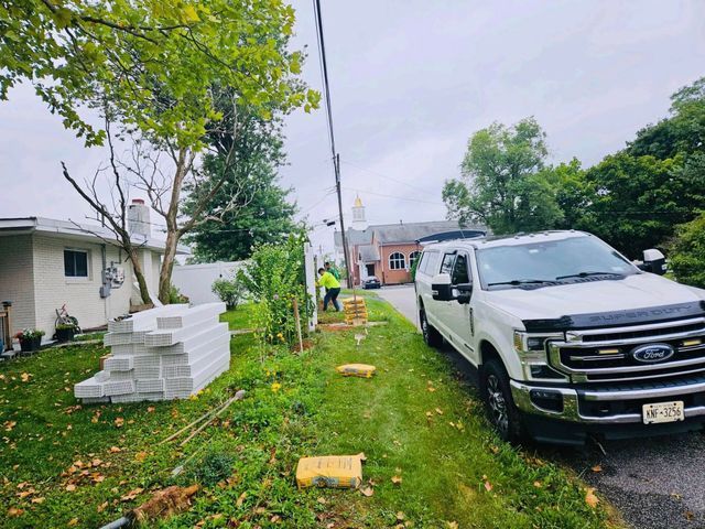 A white pickup truck parked by a grassy yard with stacked white materials and trees in the background.