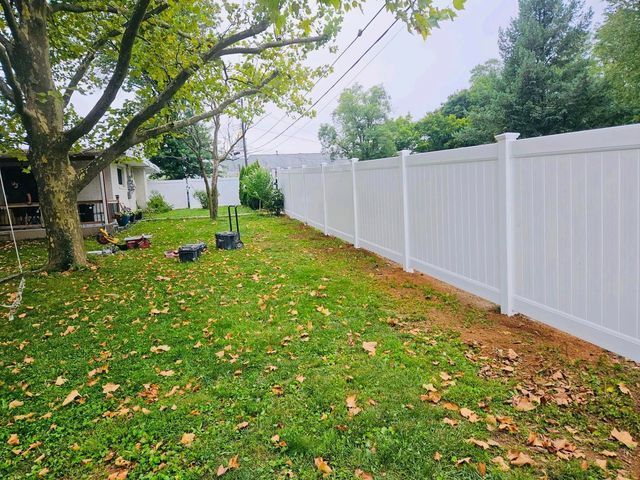 Backyard lawn with scattered leaves, trees, and a white privacy fence along the right side