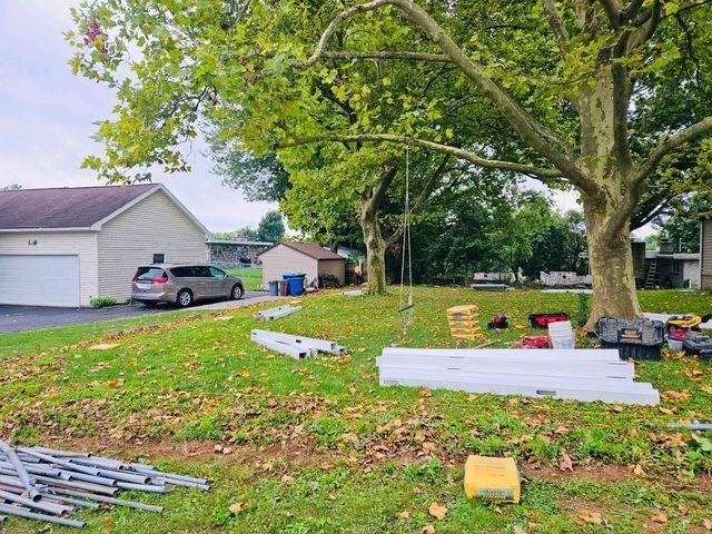 Yard cleanup with scattered metal poles and tools beneath a large tree beside a house and driveway