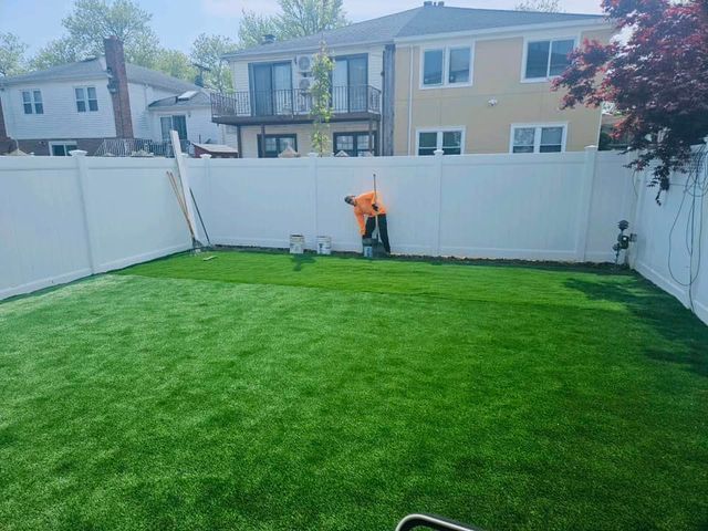 Backyard with bright green lawn, white fence, and a person in an orange shirt near the back gate