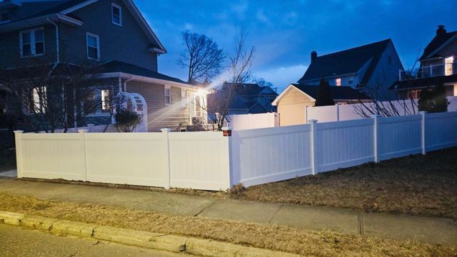Snow-covered suburban houses behind a white vinyl fence at dusk