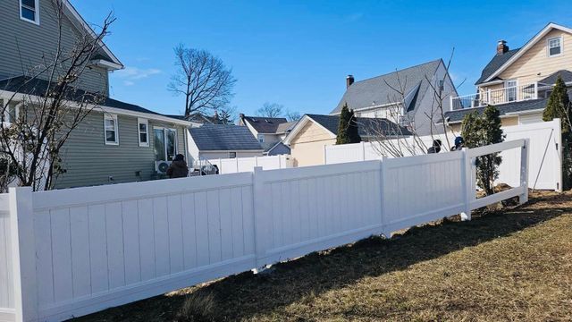 White vinyl privacy fence along a grassy backyard between suburban houses under a clear blue sky