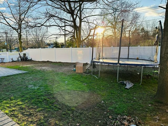 Backyard with trampoline, tree, white fence, and setting sun