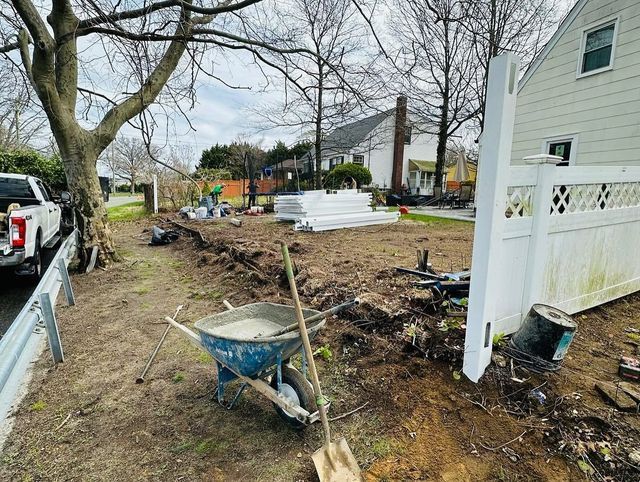 Yard under construction with wheelbarrow, dirt piles, and stacked white fencing beside a house
