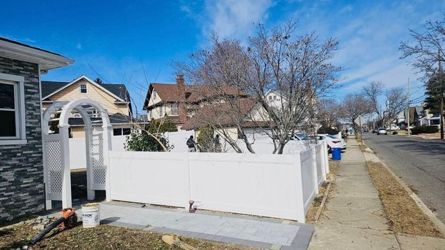 Residential sidewalk with white fence and archway beside houses on a sunny street