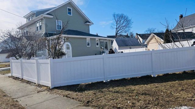 White vinyl fence along a residential corner lot beside a beige house on a sunny day