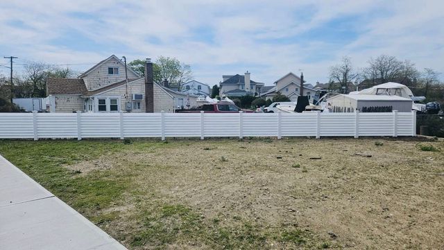 Backyard with patchy grass, concrete path, and a white fence in front of neighboring houses.