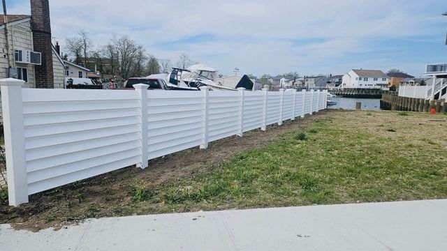 Long white vinyl fence along a grassy lot beside a house and sidewalk under a cloudy sky