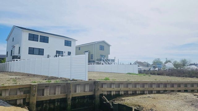 White coastal houses beside a wooden boardwalk over a rocky shoreline under a cloudy sky
